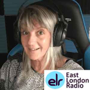 Woman in 50s grey/blond thin hair straight black and white top sitting down with headphones on. Smiling